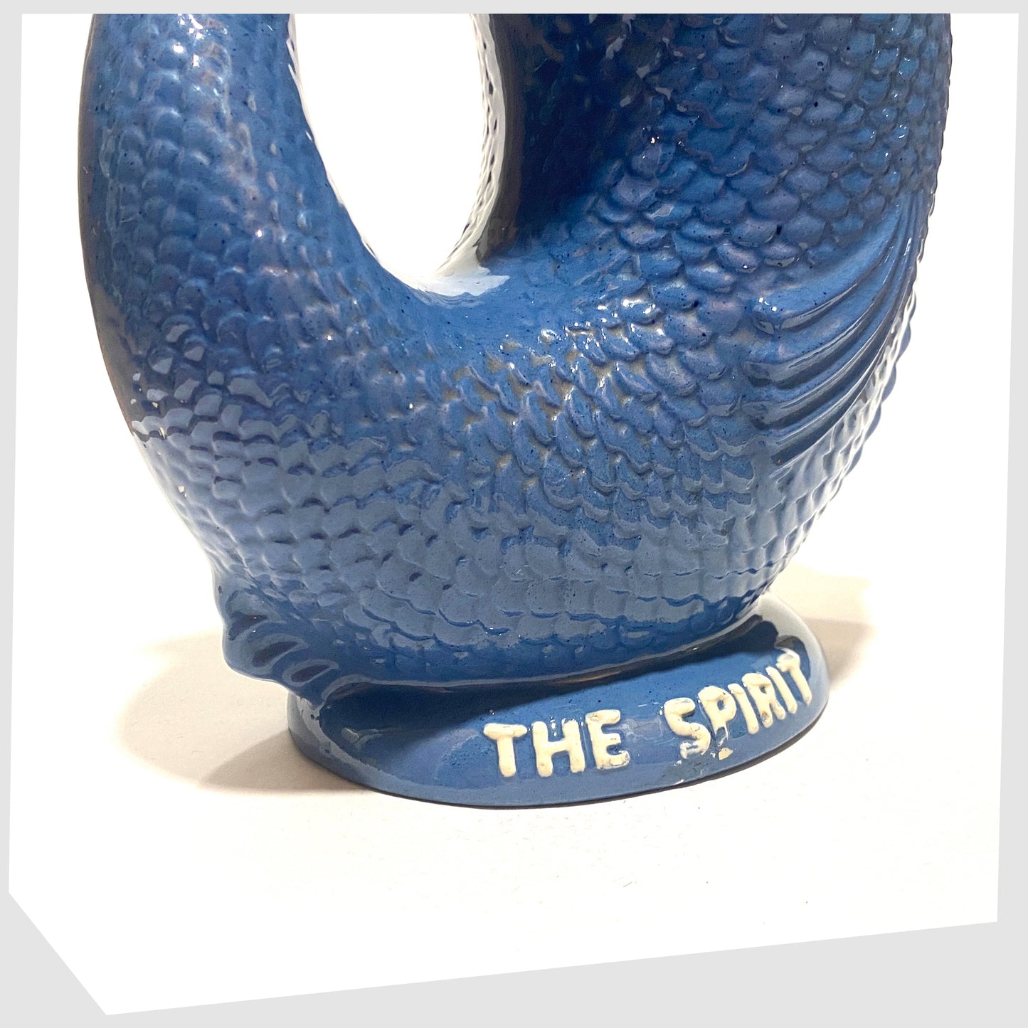 Base rim of the Dartmouth Pottery Plymouth Gin Gluggle in a sea blue glaze with white text around the spout and base