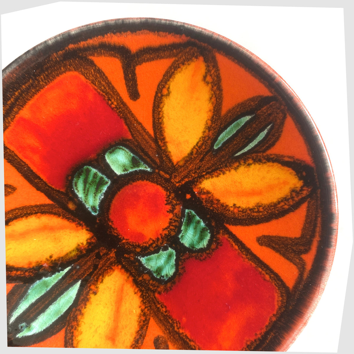 Close up of the Poole Pottery Delphis Pin Dish, shape 49, by Janet Laird glazed in a vivid orange with fluid forms of green and yellow glaze- Shown on a white background