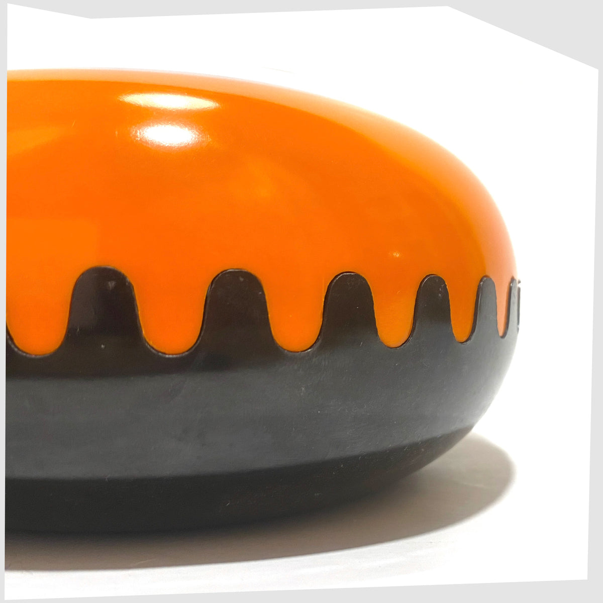 Close up of the Clam Ashtray designed by Alan Fletcher for Pentagram Design in half orange and half black, shown on a white background
