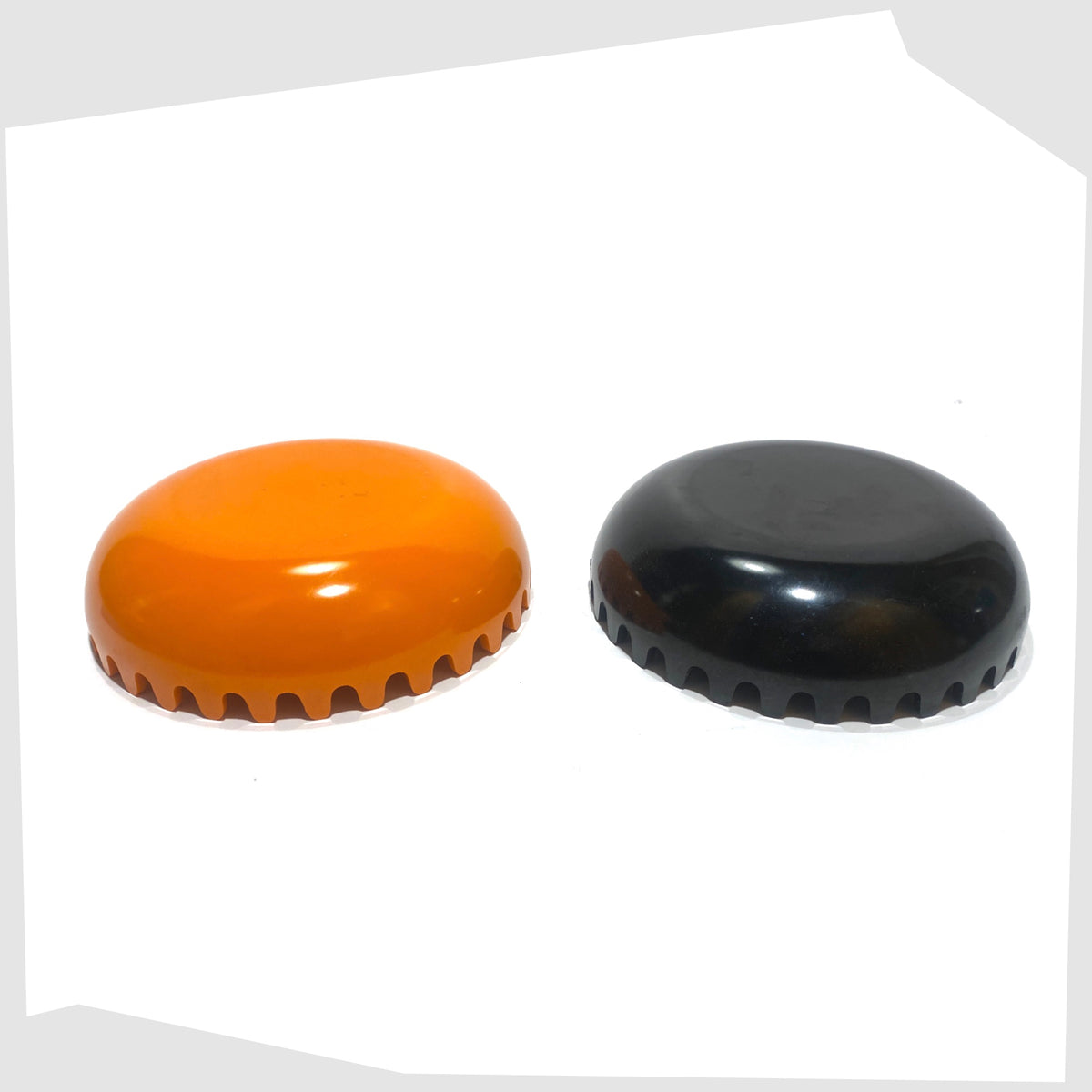 The two parts of the Clam Ashtray designed by Alan Fletcher for Pentagram Design in half orange and half black, shown on a white background