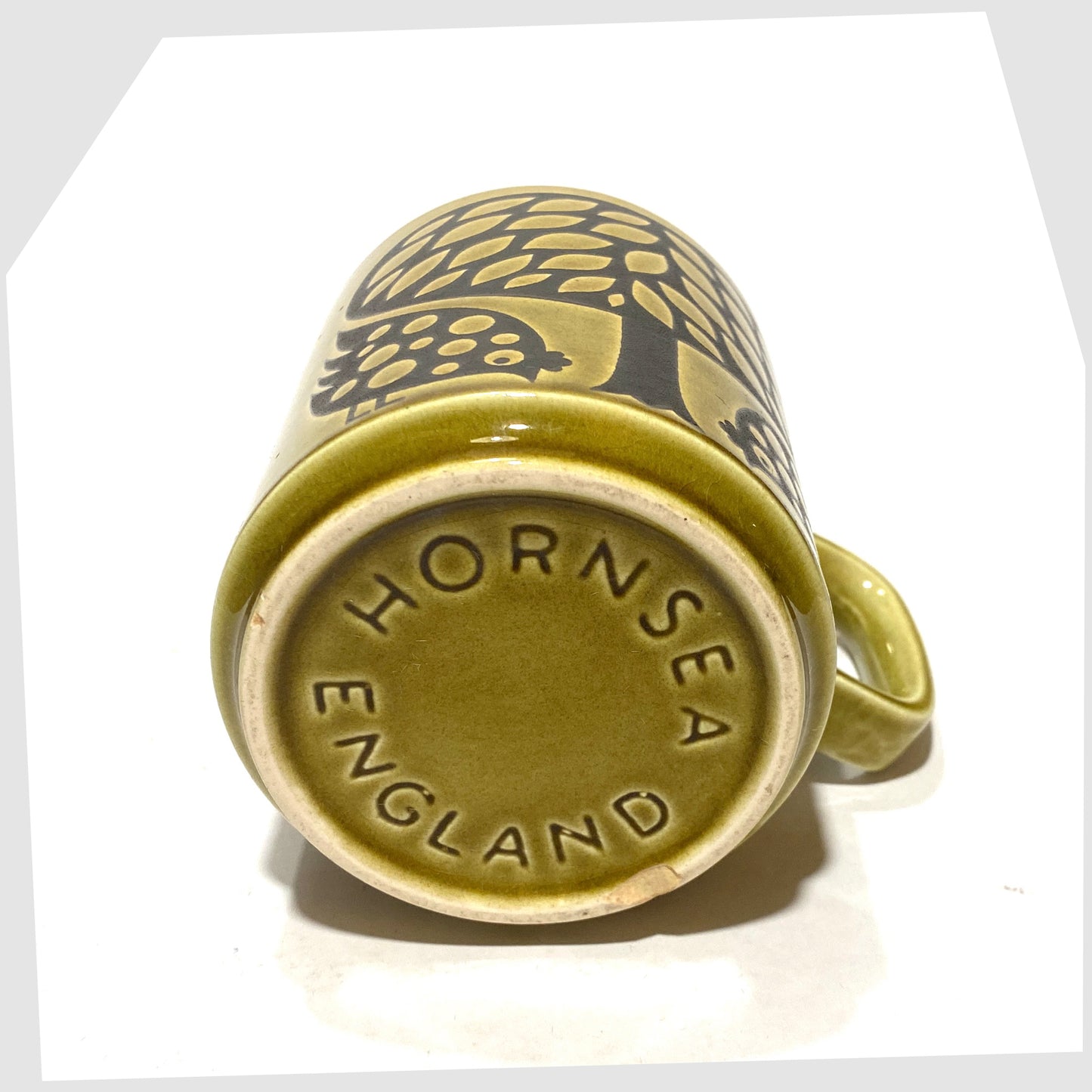 Base of the Original Hornsea Pottery Mug featuring a pair of partridge birds at the base of a tree, in an olive green glaze with lack decals, shown on a white background