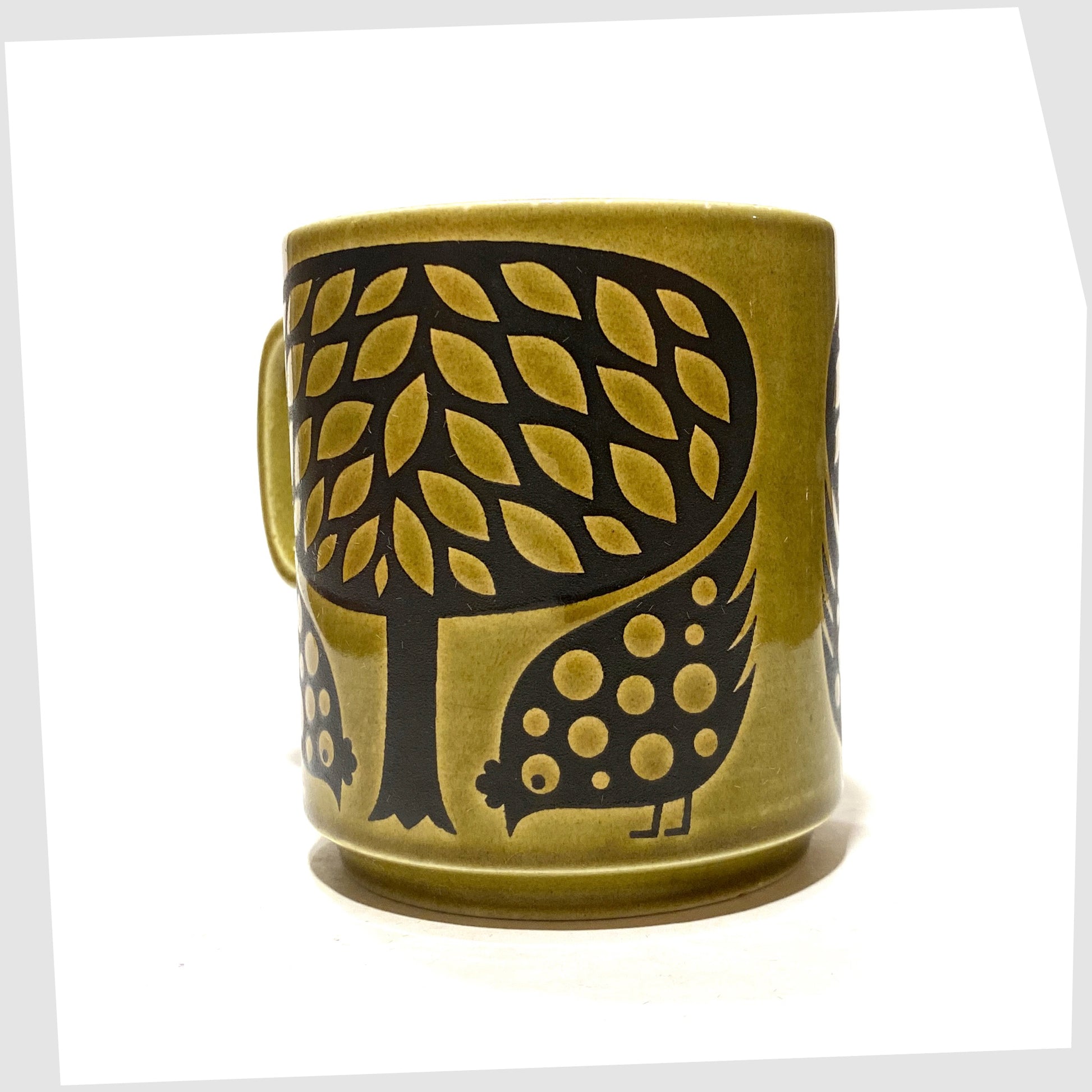Original Hornsea Pottery Mug by John Clappison featuring a pair of partridge birds at the base of a tree, in an olive green glaze with lack decals, shown on a white background