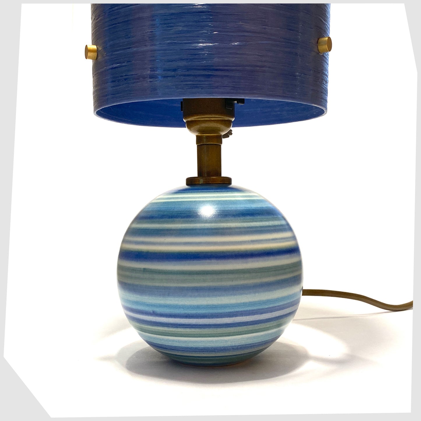 Close up of the hand-painted Jersey Pottery Spherical Table Lamp with a blue spun fibreglass lampshade, shown on a white background