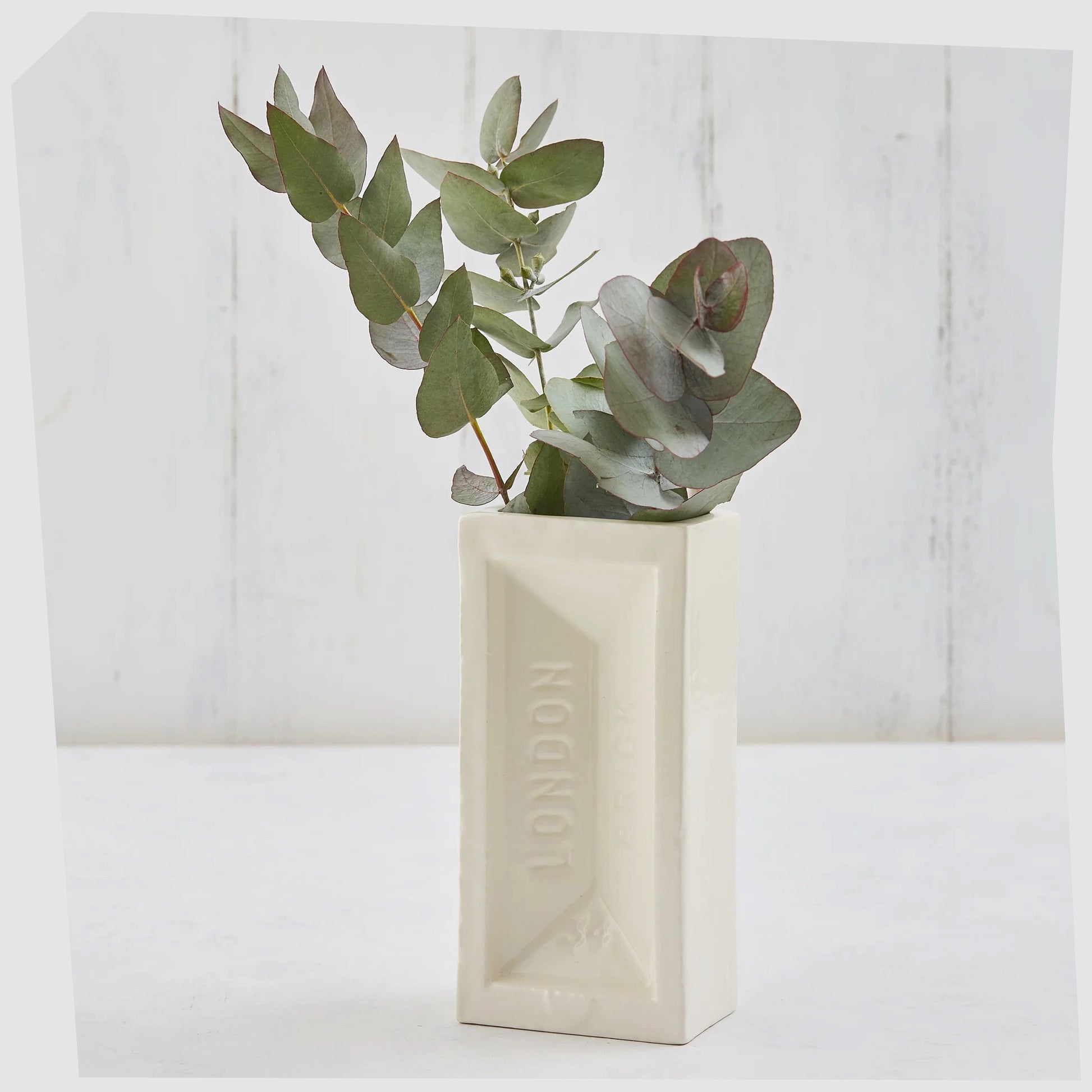 London Brick Vase in white glaze shown with a eucalyptus plant inside.