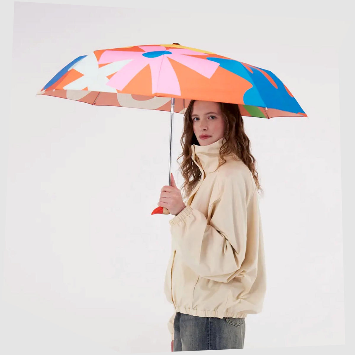 Lifestyle image of the Salsa Original Duckhead Umbrella in a red fabric with abstract and floral multicoloured shapes, shown held in a woman's hand