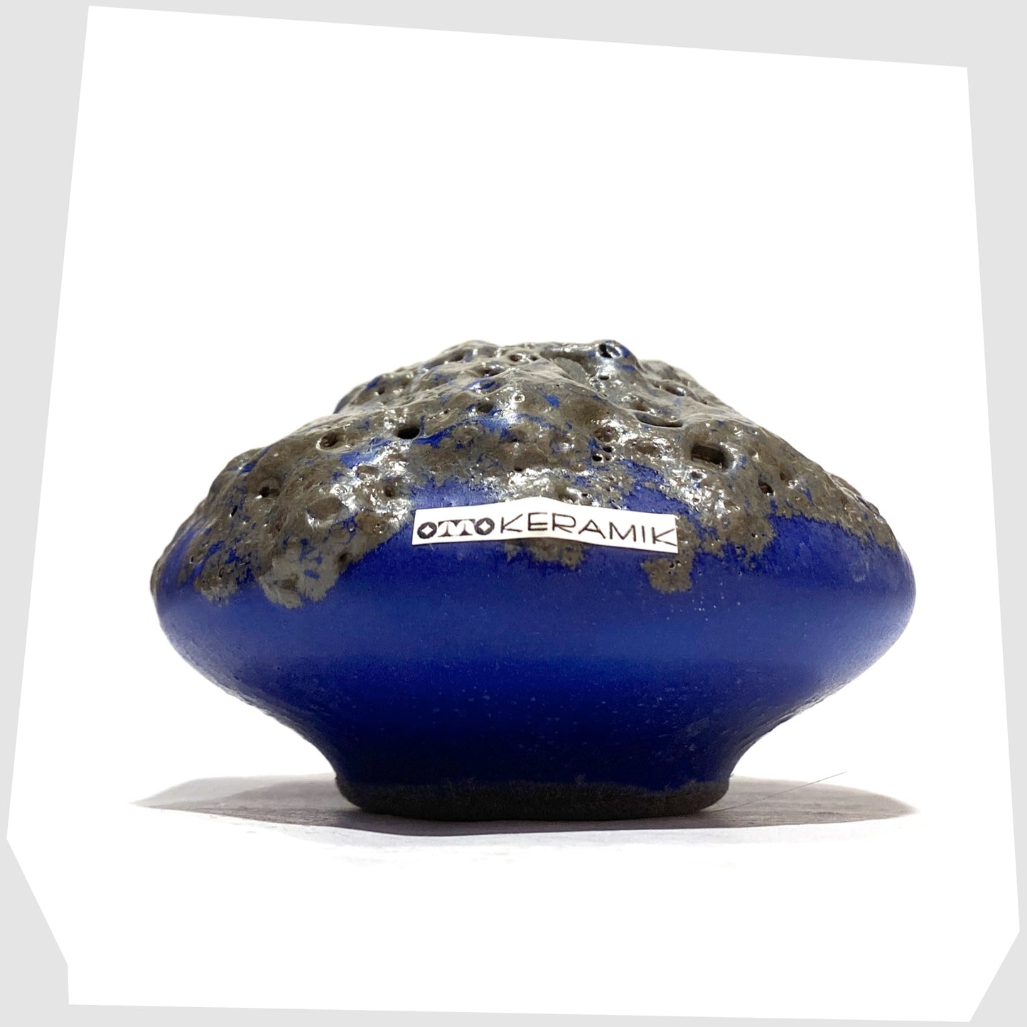 Small Otto Keramik 203 Vase in blue glaze with grey fat lava glazing, shown with the Otto Keramik label attached, shown on a white background