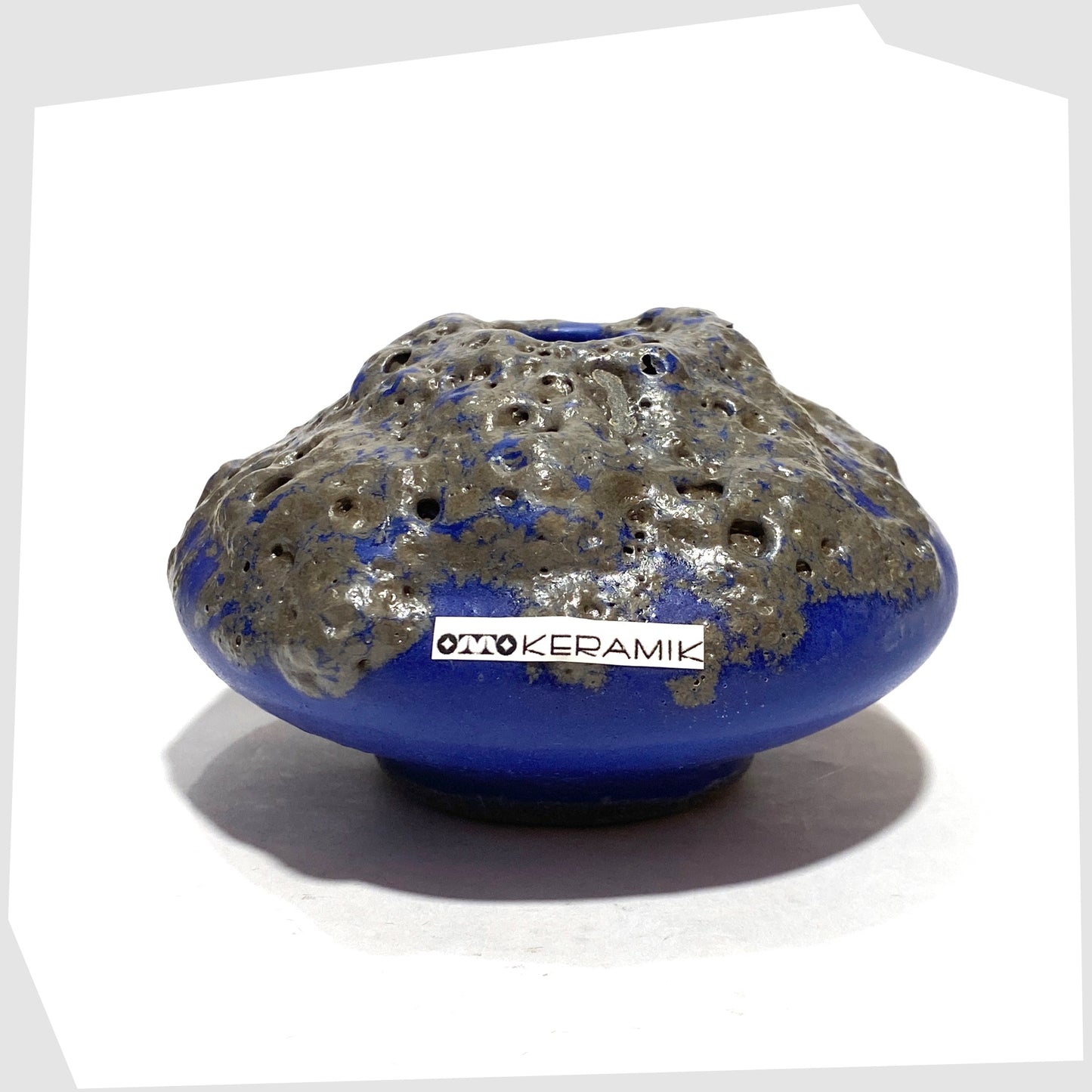 Compact Otto Keramik 203 Vase in blue glaze with grey fat lava glazing, shown with the Otto Keramik label attached, shown on a white background