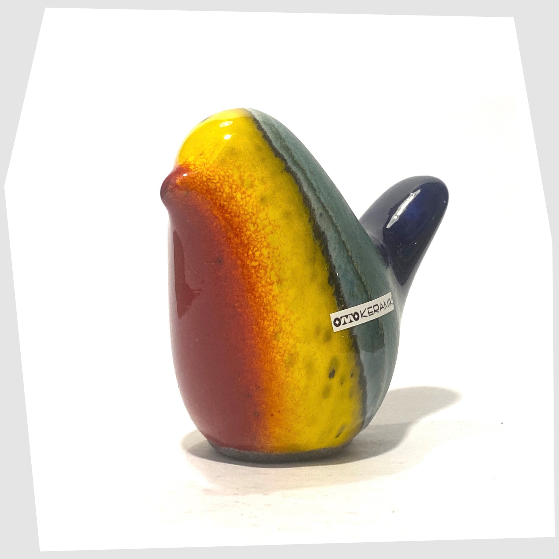 ceramic bird by otto keramik in multicoloured rainbow glaze of red, yellow, green and dark blue, shown on a hite background