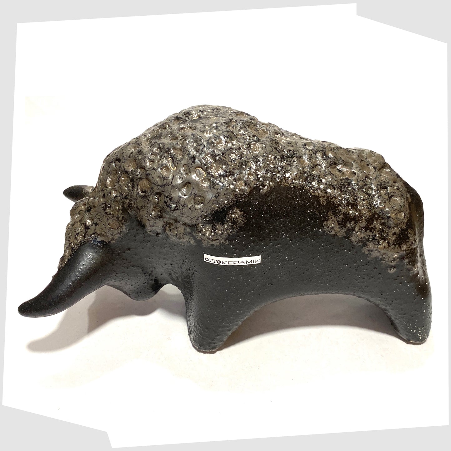 Overhead view of the Otto Keramik Bull in textured black glaze with deep fat lava glazing along the spine, shown on a white background