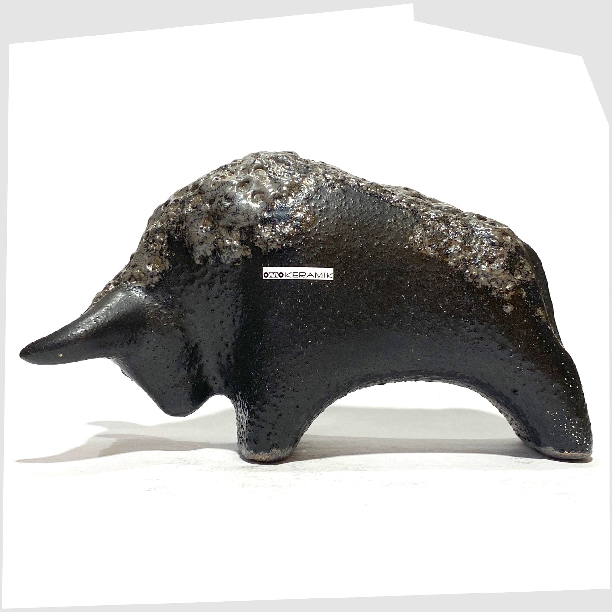 Otto Keramik Bull in textured black glaze with deep fat lava glazing along the spine, with original retail sticker attached, shown on a white background