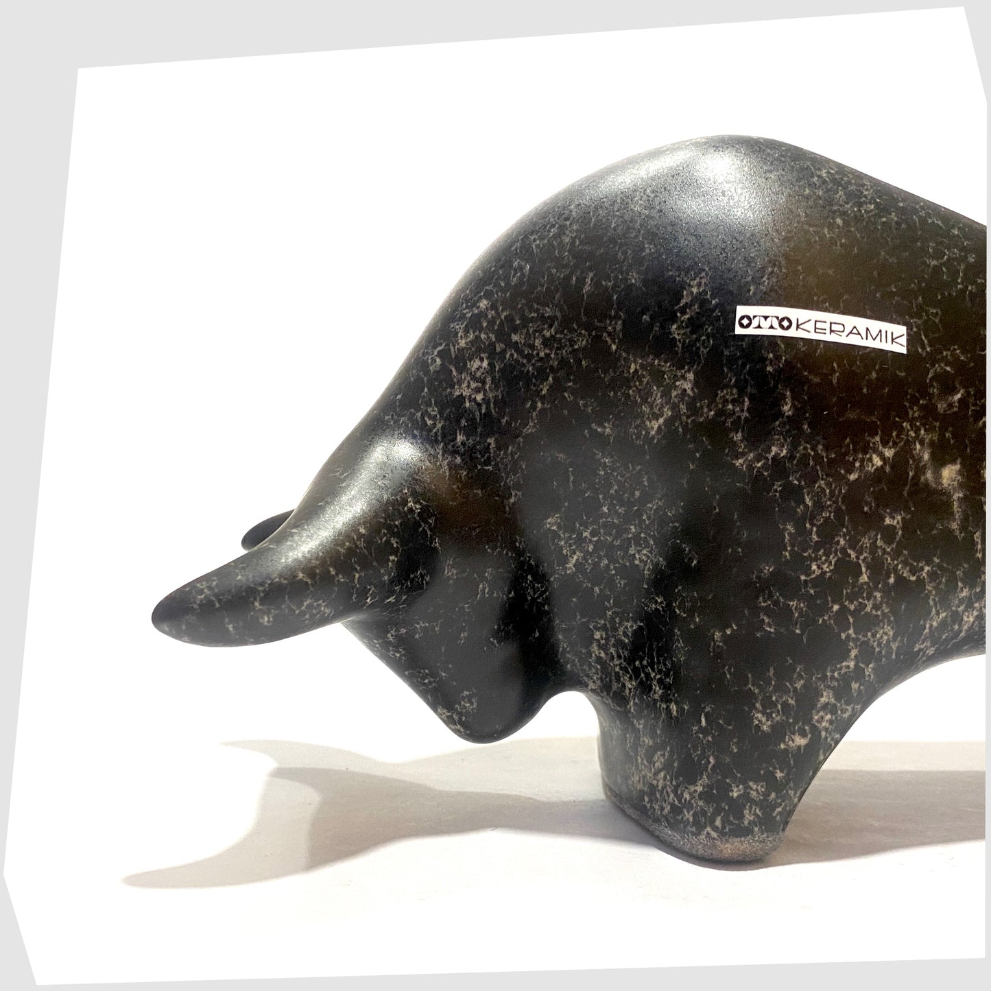 Close up of the Otto Keramik ceramic bull-shaped figurine in black speckled glaze, shown on a white background