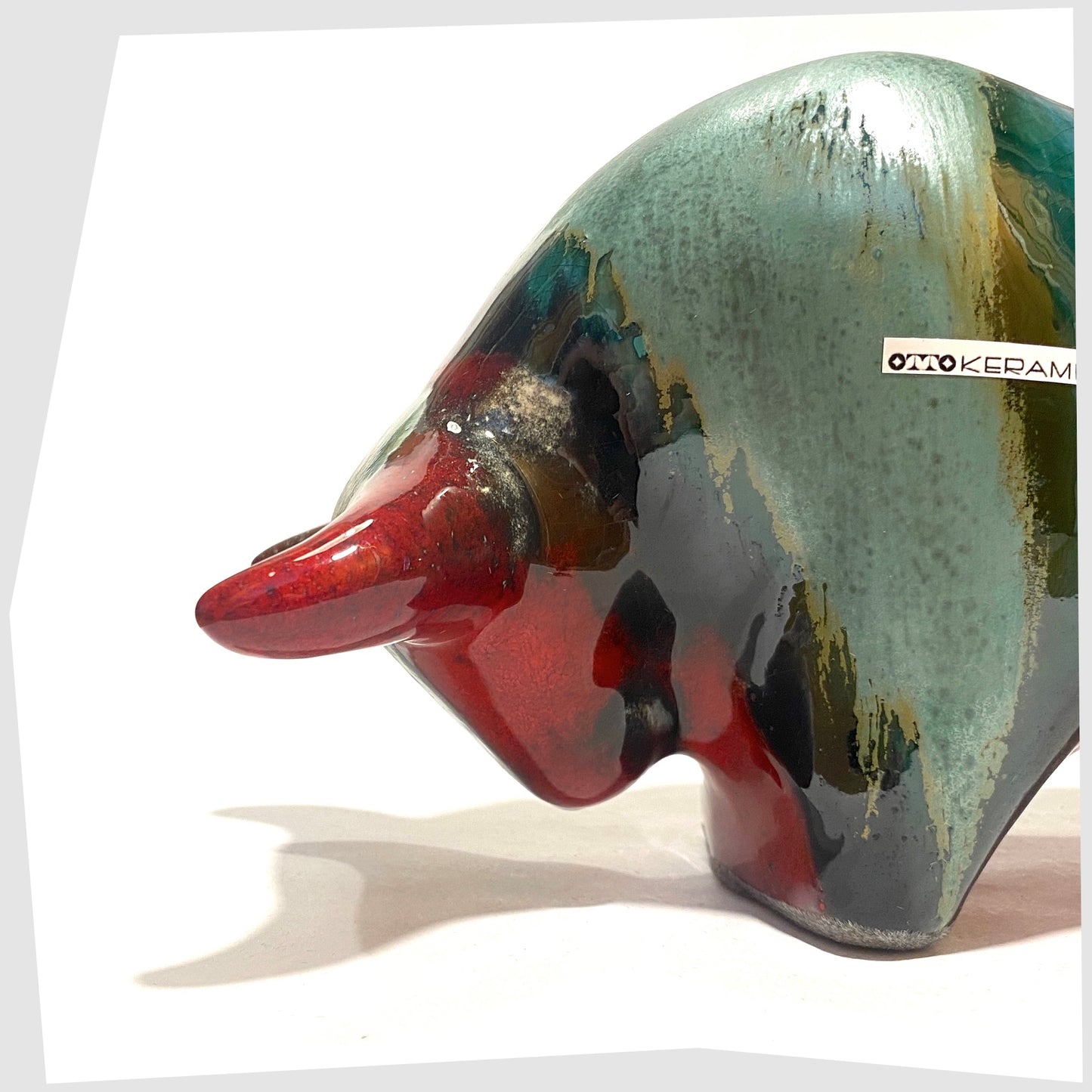 Close up of the front of the Otto Keramik Bull in Bolivia glaze of deep red with stripes of rich sea green, shown on a white background