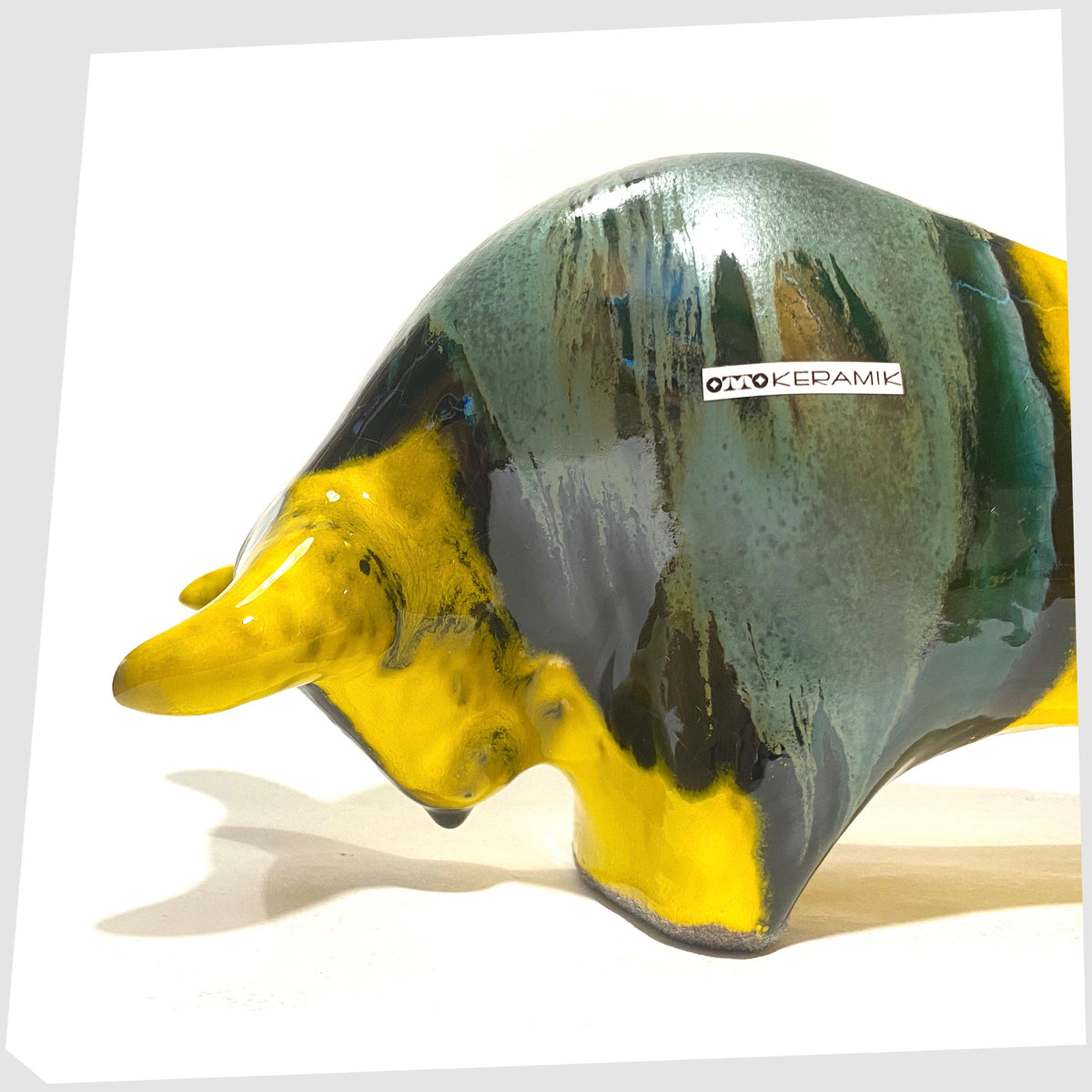 Close up of the Otto Keramik Ceramic Bull in Brazil Glaze of yellow and sea green stripes, shown on a white background
