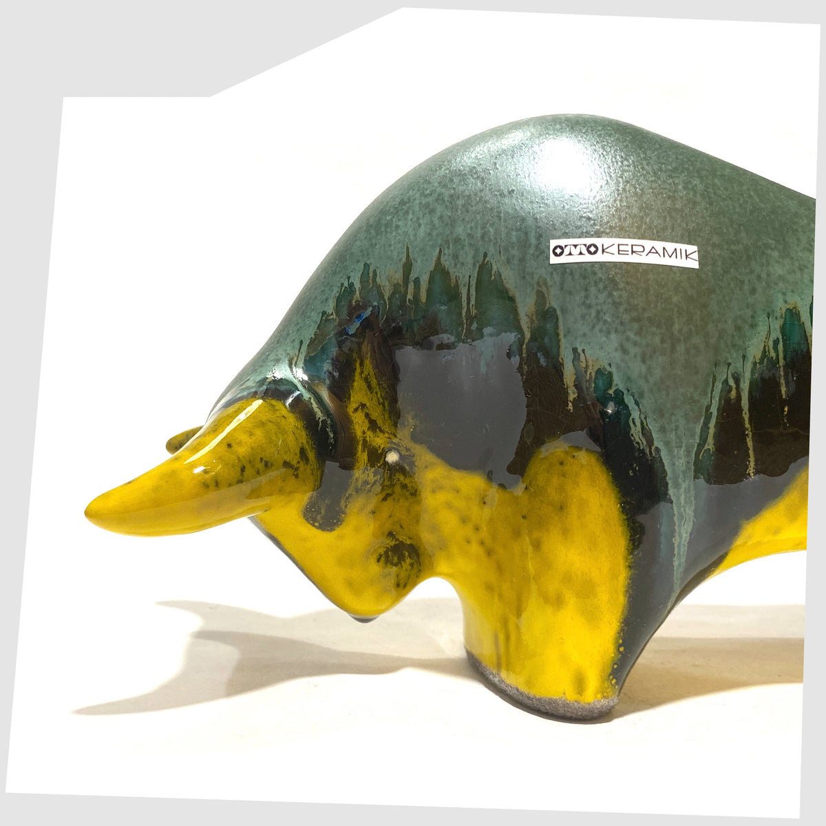 Close up of the Otto Keramik ceramic bull-shaped sculpture in green over yellow drip glaze, shown on a white background