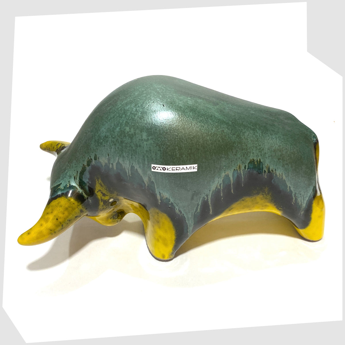 Angled view of the Otto Keramik ceramic bull-shaped sculpture in green over yellow drip glaze, shown on a white background
