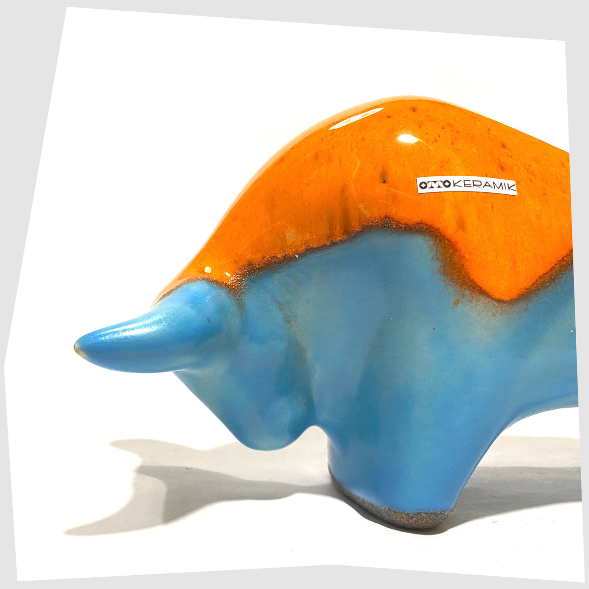 Close up of the Otto Keramik Bull in orange over blue glaze, shown on a white background