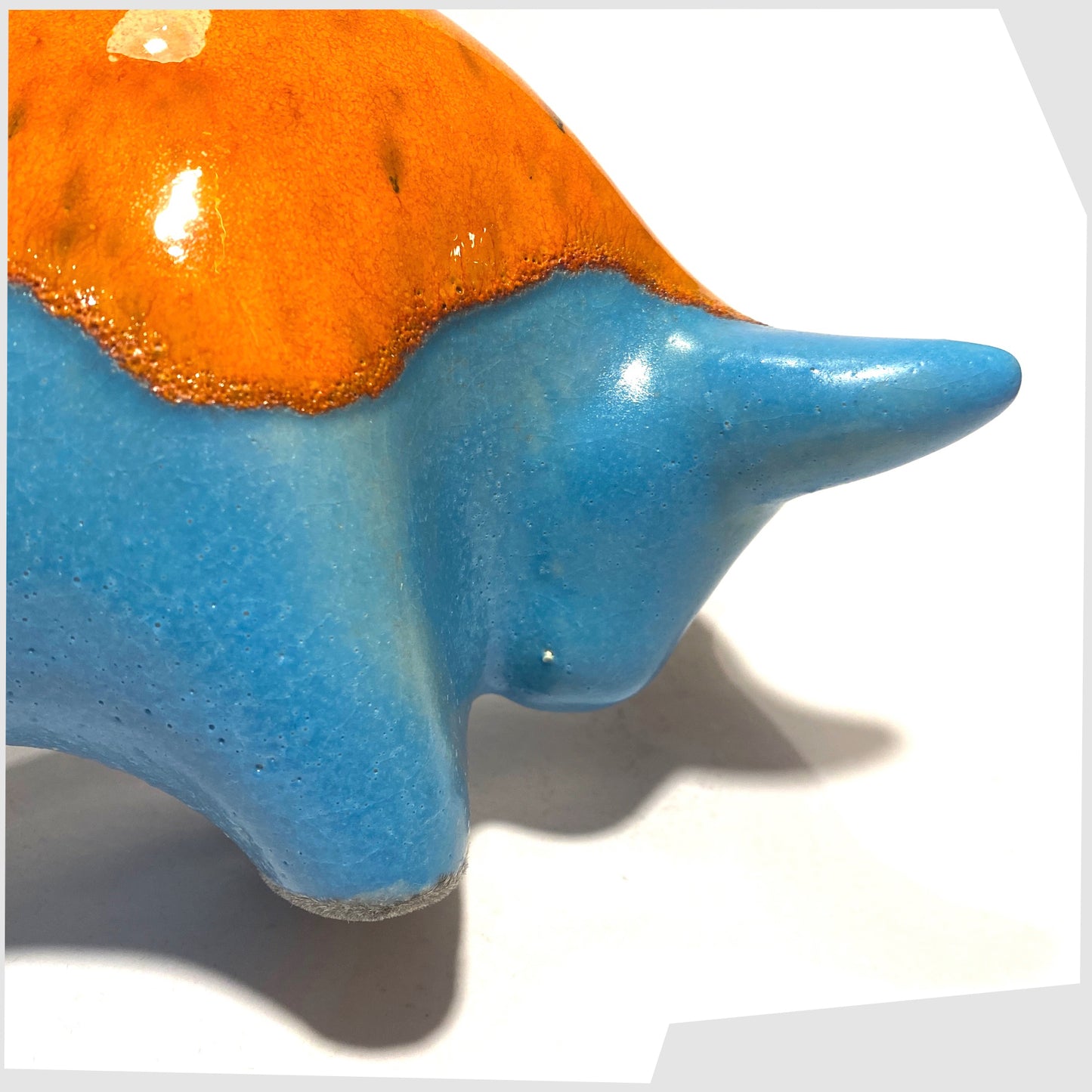 Clode up of the front of the Otto Keramik Ceramic Bull in Orange Over Blue glaze, shown on a white background