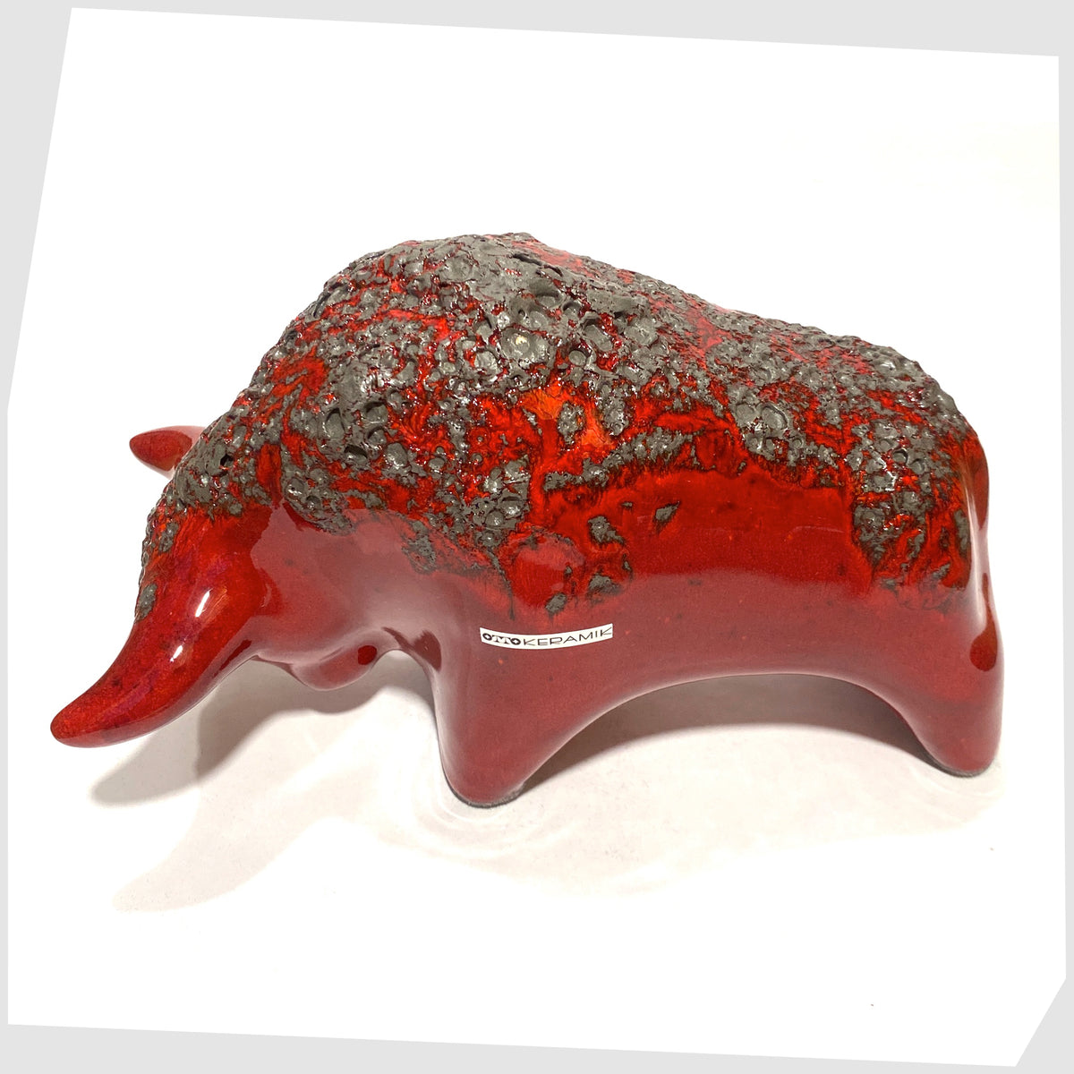 Back of the Otto Keramik ceramic bull in red fat lava glaze, bull shaped sculpture in red with grey fat lava along the spine, shown on a white background
