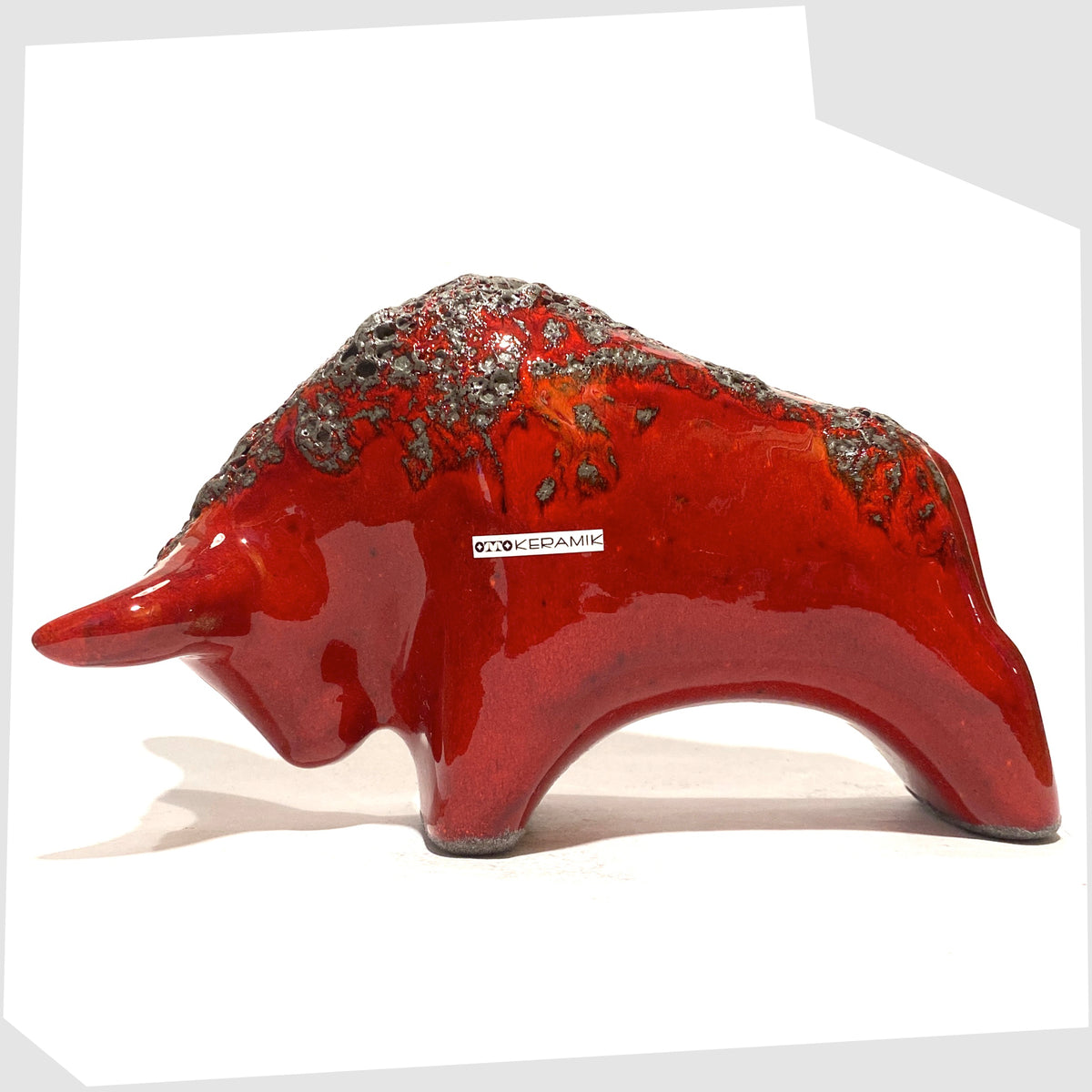 Otto Keramik ceramic bull in red fat lava glaze, bull shaped sculpture in red with grey fat lava along the spine, shown on a white background