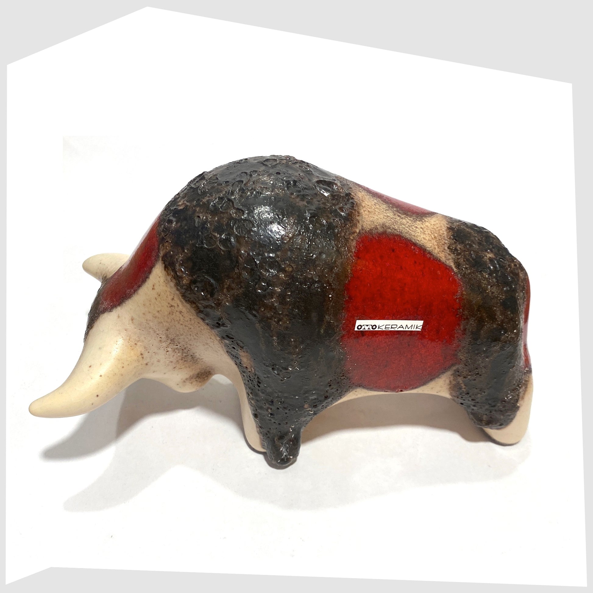 Back of the Otto Keramik ceramic bull in cream and red glaze with bands of thick fat lava, shown on a white background