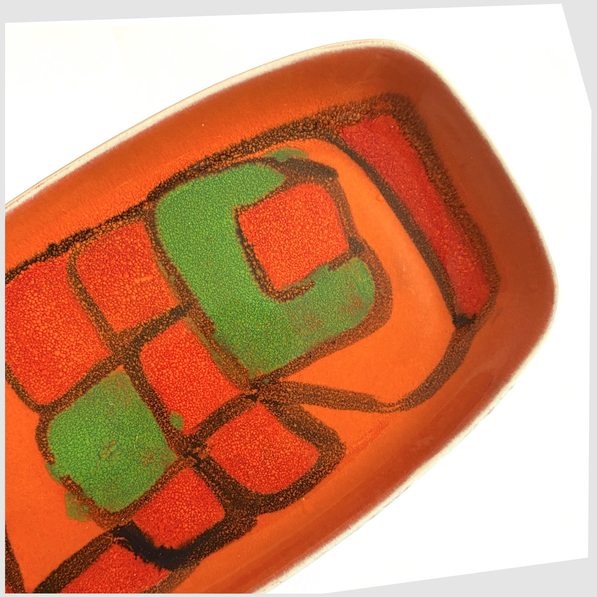 Close up of the Poole Pottery Delphis Dish, Shape 61, by Gillian Taylor in a vivid orange glaze with forms of green and red, photographed on a white background
