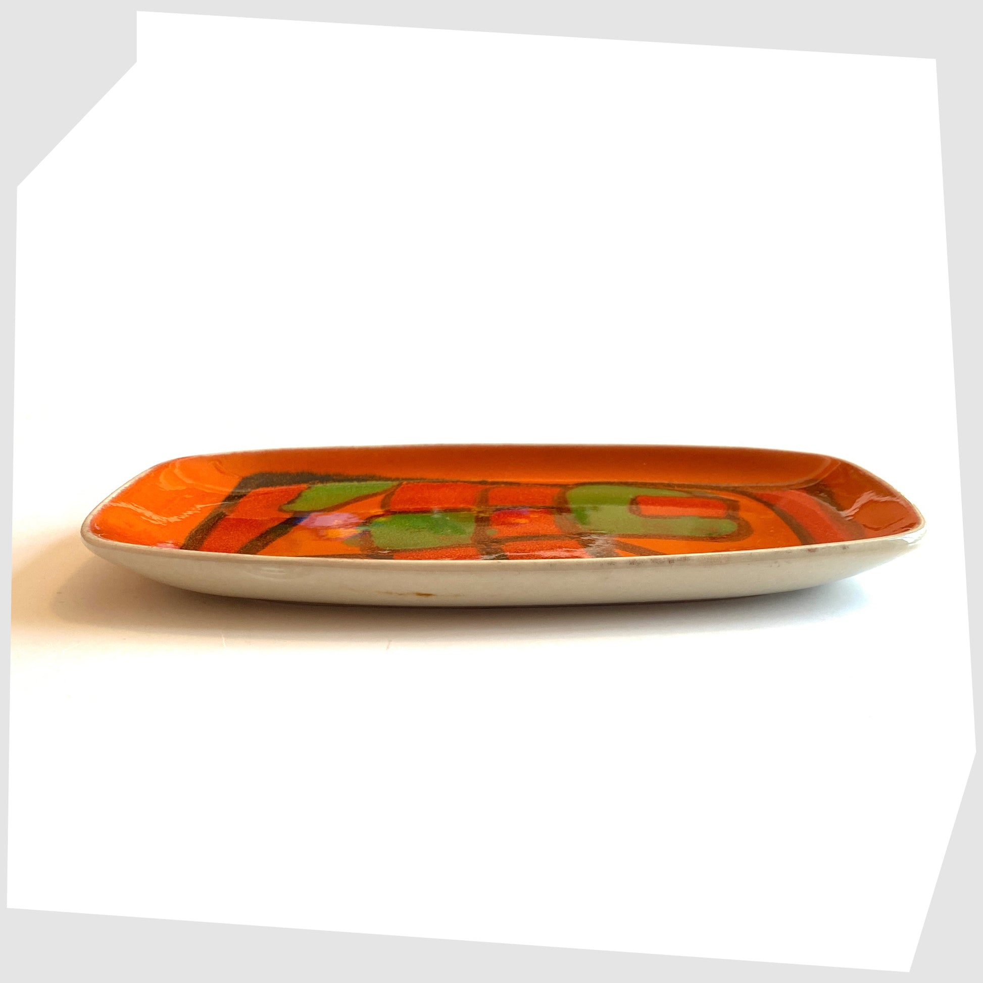 Side profile of the Poole Pottery Delphis Dish, Shape 61, by Gillian Taylor in a vivid orange glaze with forms of green and red, photographed on a white background