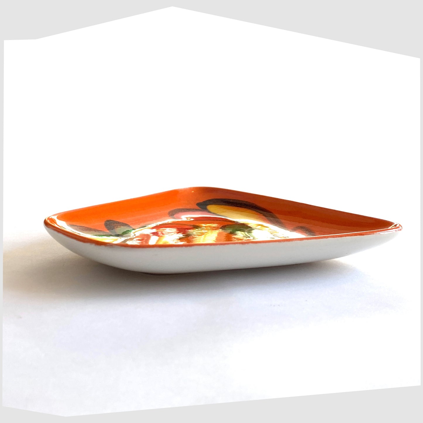 side angle of the Poole Pottery Delphis Dish, shape 81, by paintress Mary Albon in a vivid orange glaze with fluid forms of red, green and yellow
