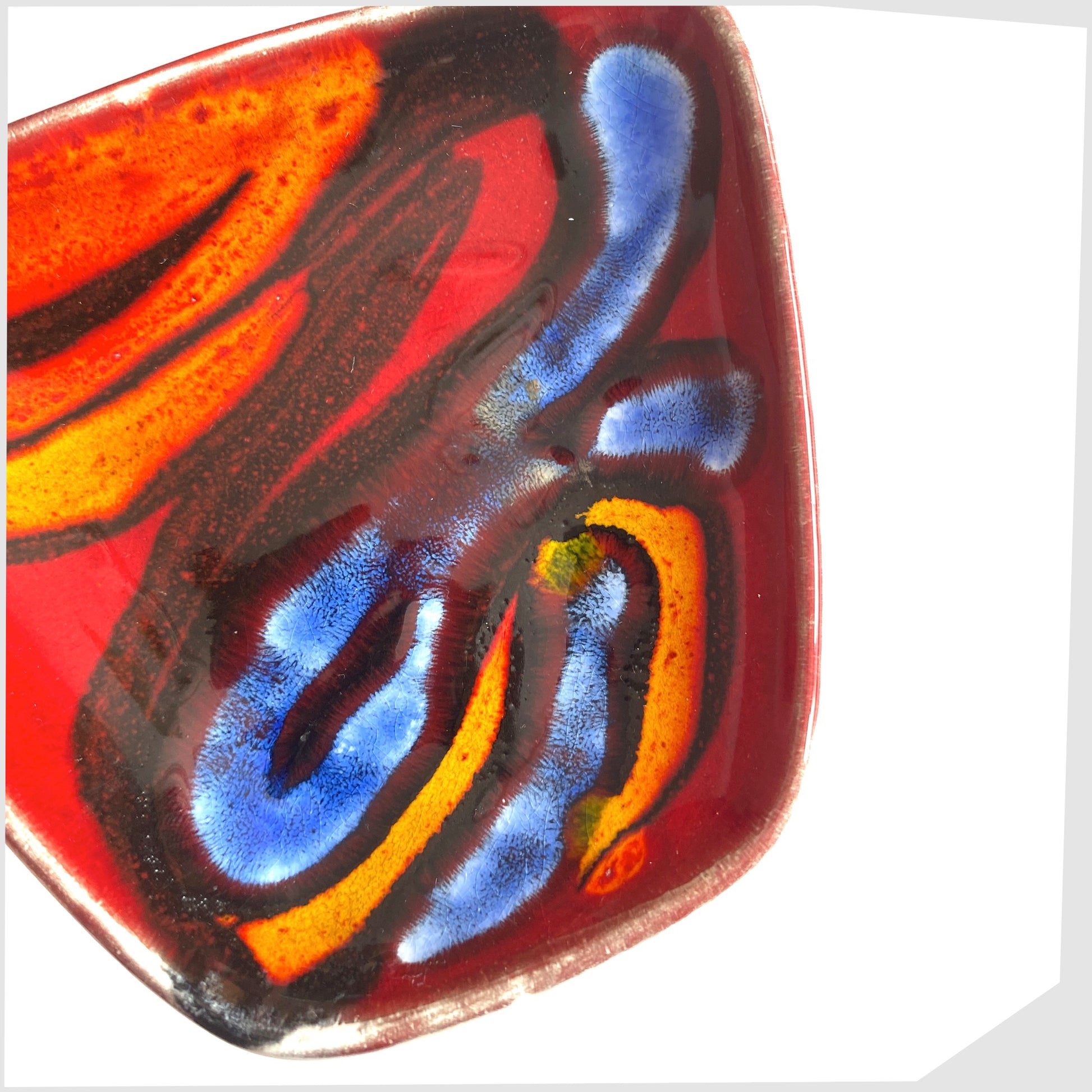 close up of the Poole Pottery Delphis Pin Dish, shape 41, by Loretta Leigh glazed in a rich red with fluid forms of blue, orange and yellow