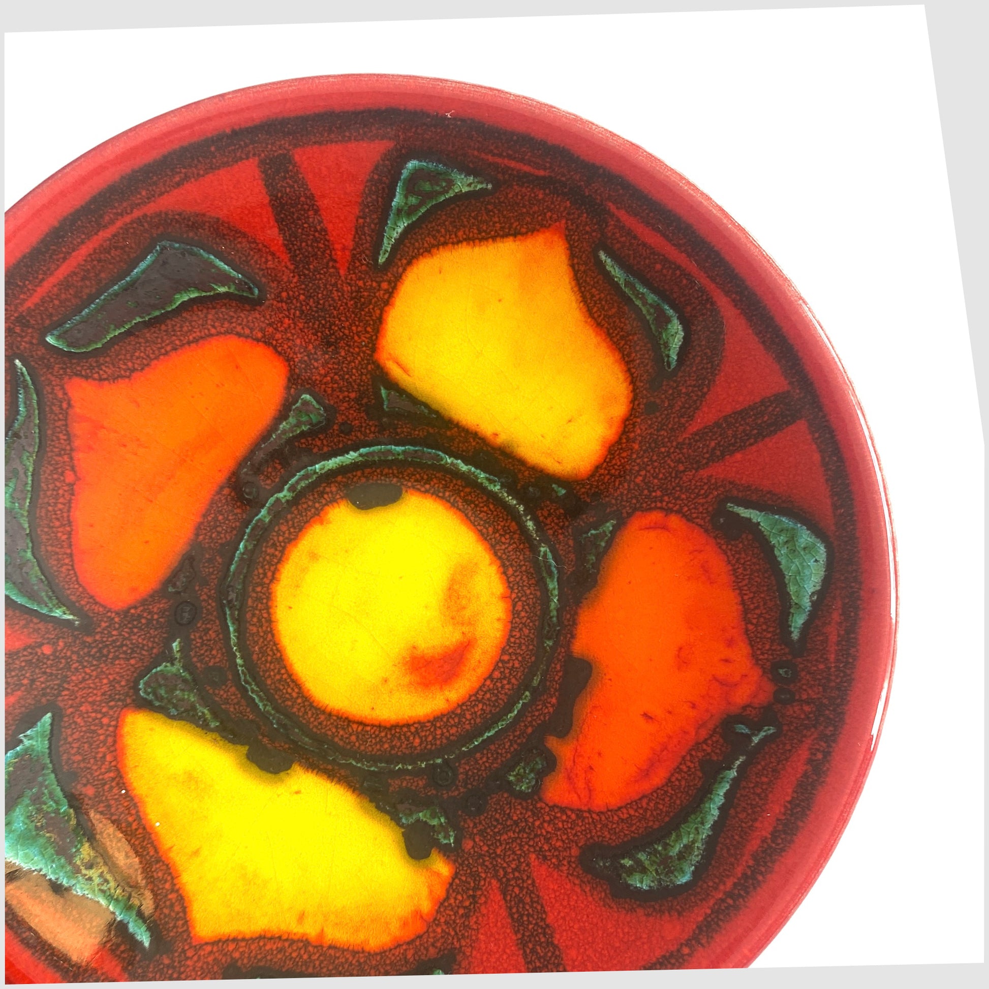 Close up of the Poole Pottery Delphis Pin Dish by Janet Laird in a vibrant red glaze with radiating forms of rich yellow and green, shown on a white background