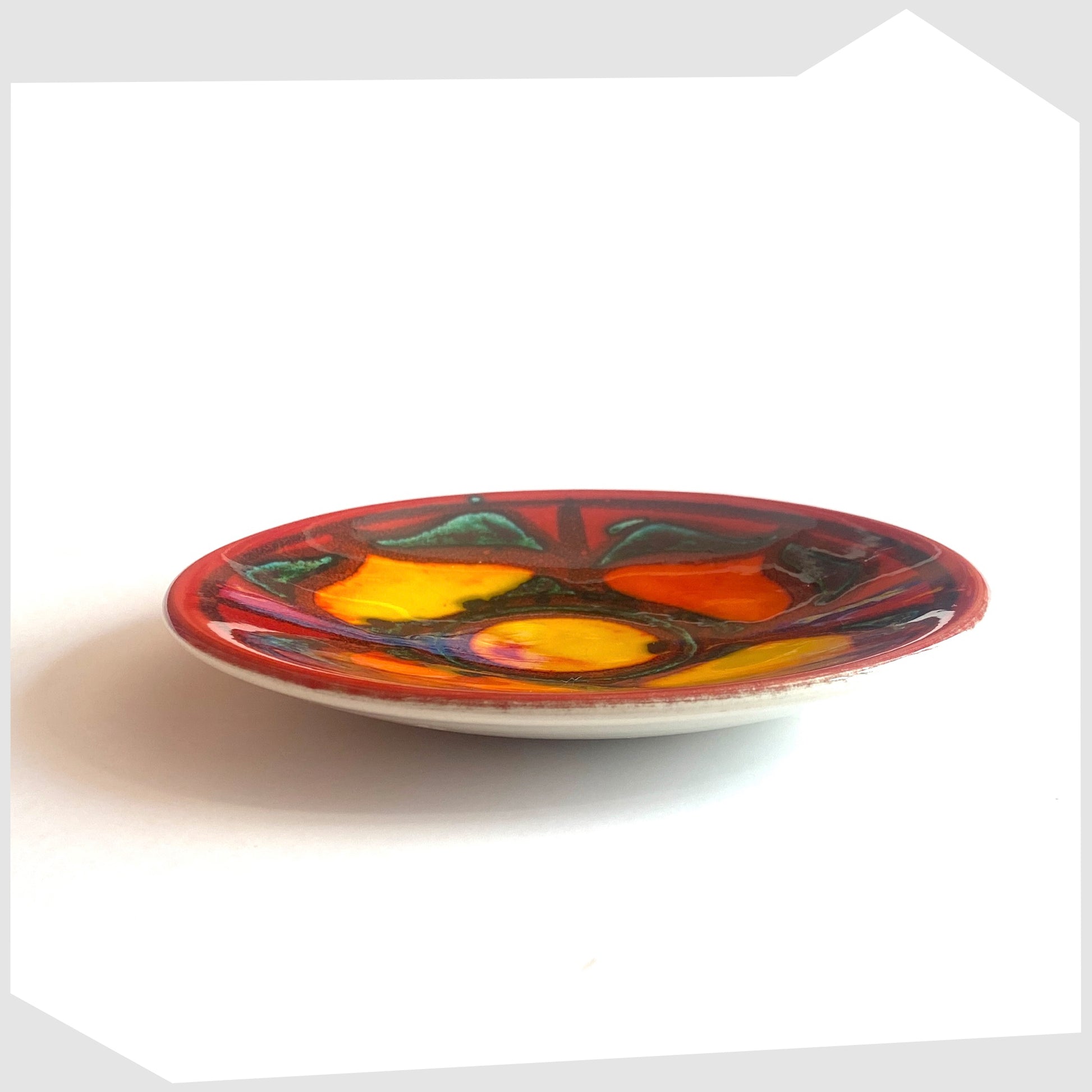 Side profile of the Poole Pottery Delphis Pin Dish by Janet Laird in a vibrant red glaze with radiating forms of rich yellow and green, shown on a white background