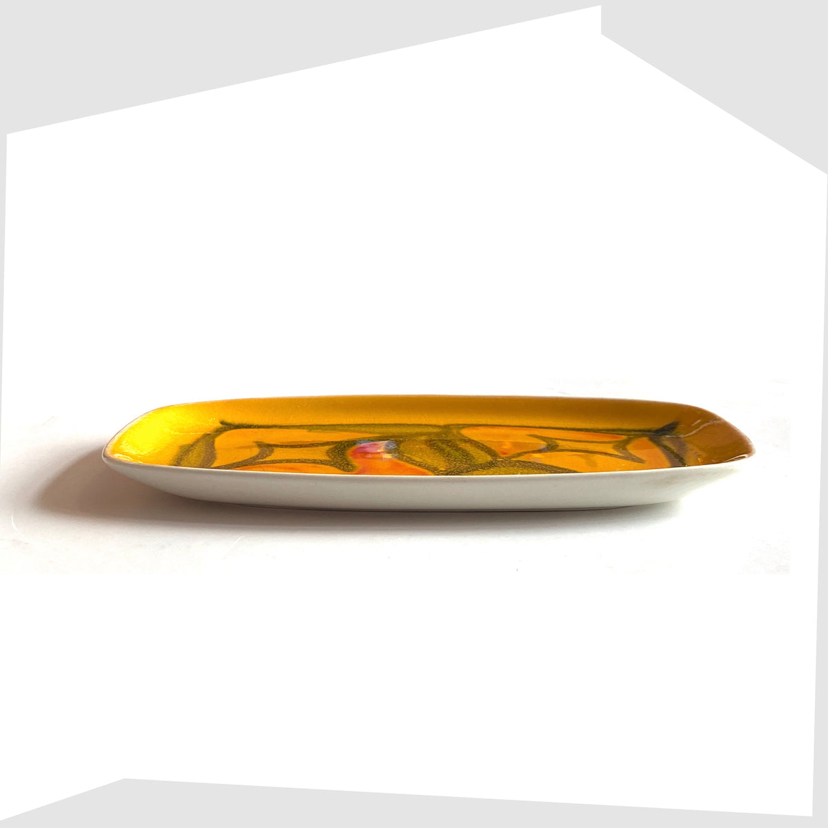 Side profile of the Poole Pottery Delphis Pin Dish, Shape 361, by Lynn Gregory in a vibrant yellow glaze with free-form shapes of orange and green, shown on a white background