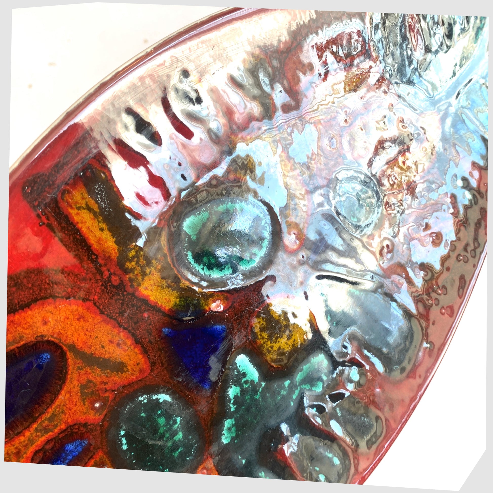 Close up showing the textured glaze of the Poole Pottery Delphis Spear Dish, Shape 82, by paintress Irene Kerton finished in a vibrant red glaze with fluid forms of orange and turquoise, shown on a white background