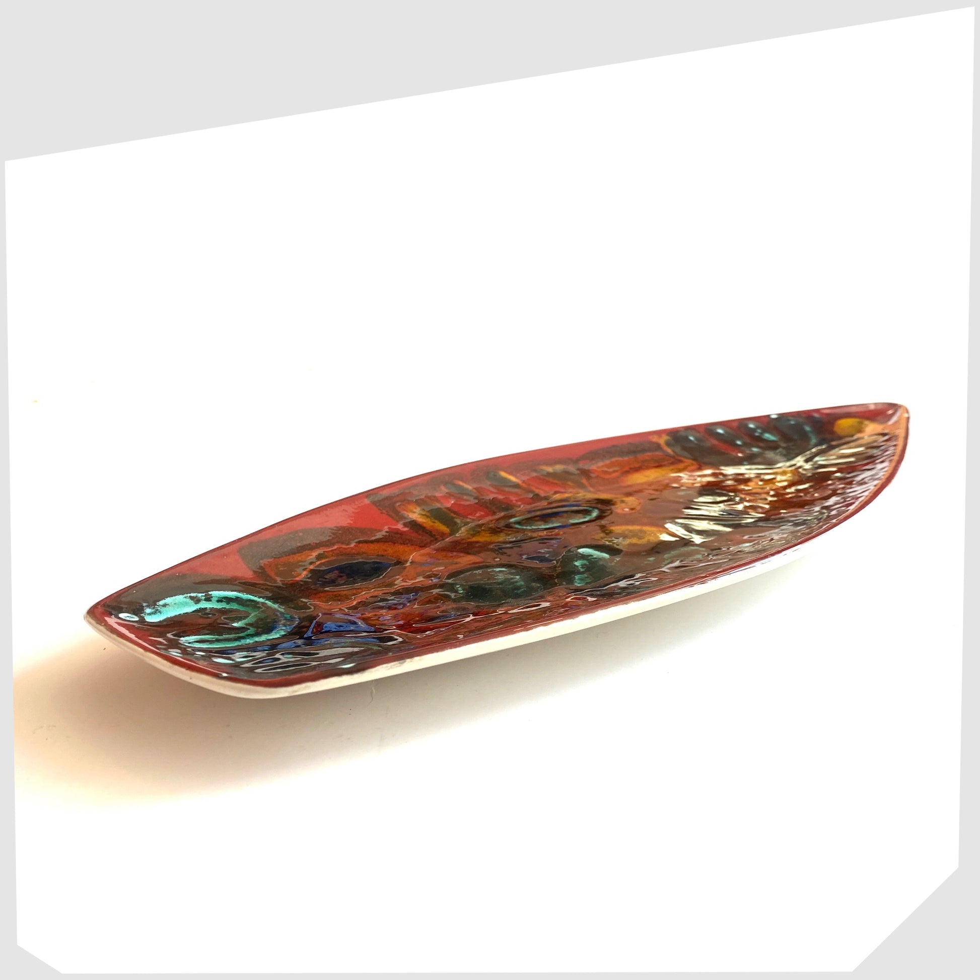 Side profile of the Poole Pottery Delphis Spear Dish, Shape 82, by paintress Irene Kerton finished in a vibrant red glaze with fluid forms of orange and turquoise, shown on a white background