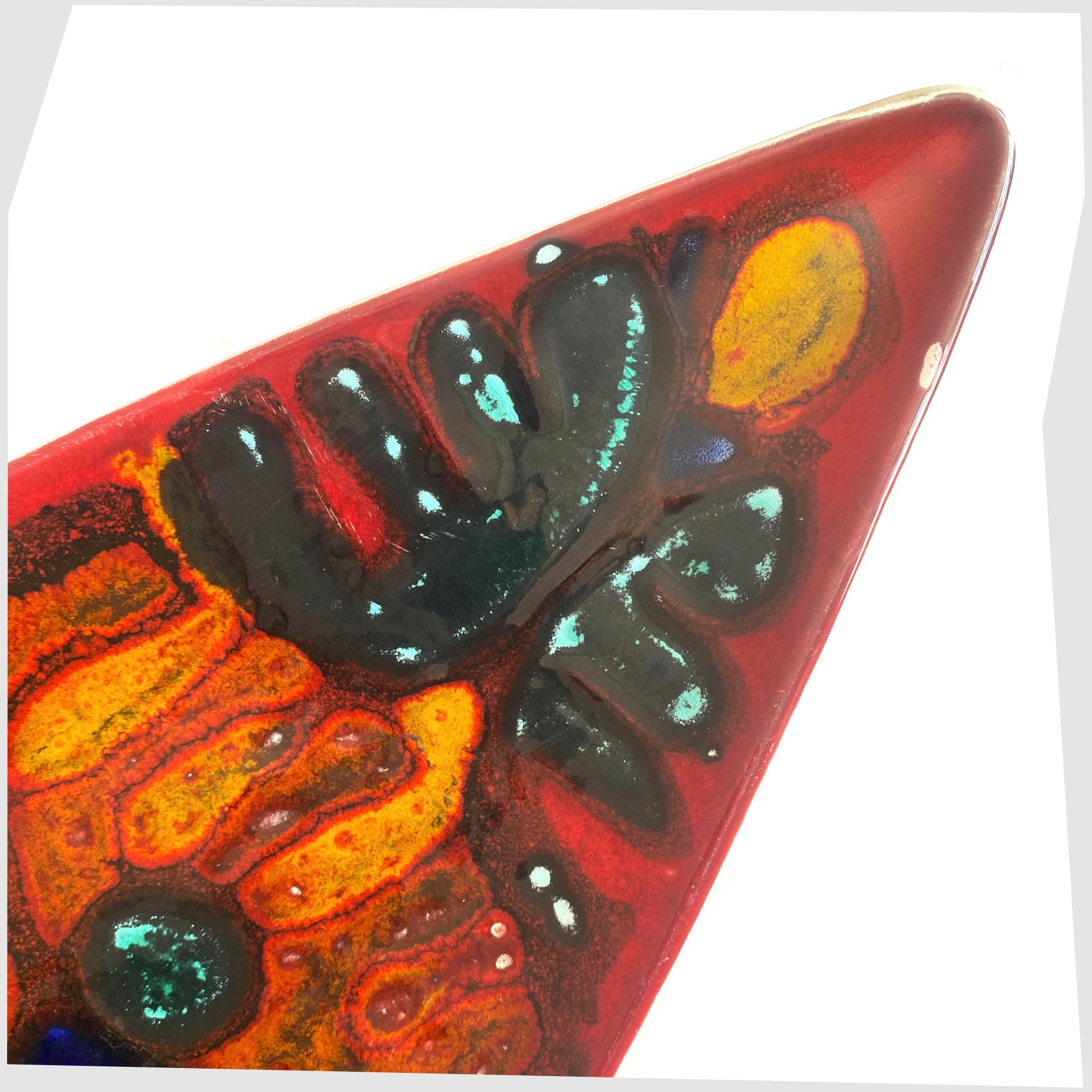 Close up of the tip of the Poole Pottery Delphis Spear Dish, Shape 82, by paintress Irene Kerton finished in a vibrant red glaze with fluid forms of orange and turquoise, shown on a white background