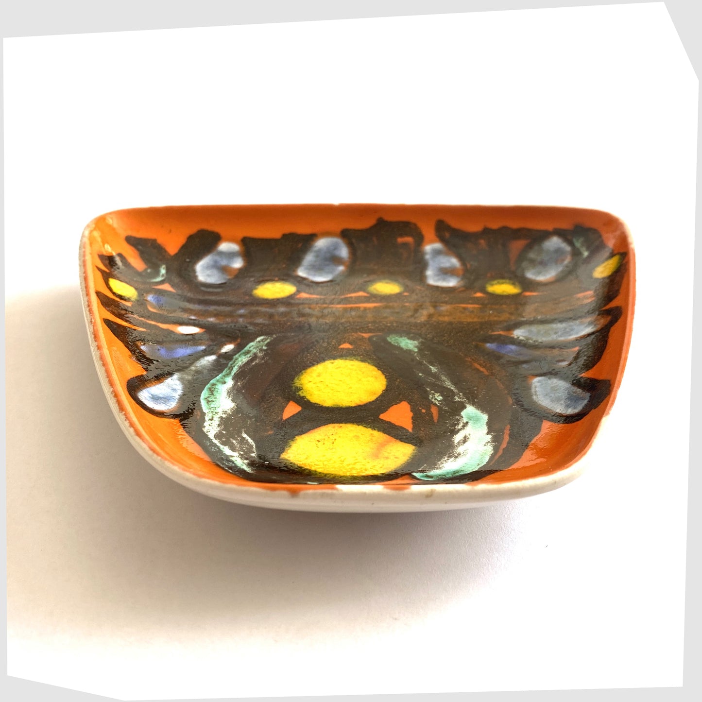 front angle of the poole pottery delphis dish, shape 81, glazed in a vibrant orange with black lines framing yellow and blue circles