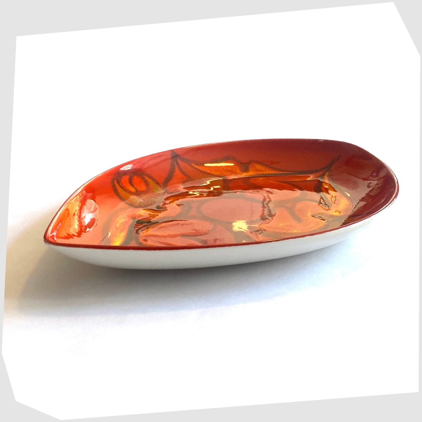 side profile of the poole pottery teardrop dish finished in a red delphis glaze with orange and green fluid forms