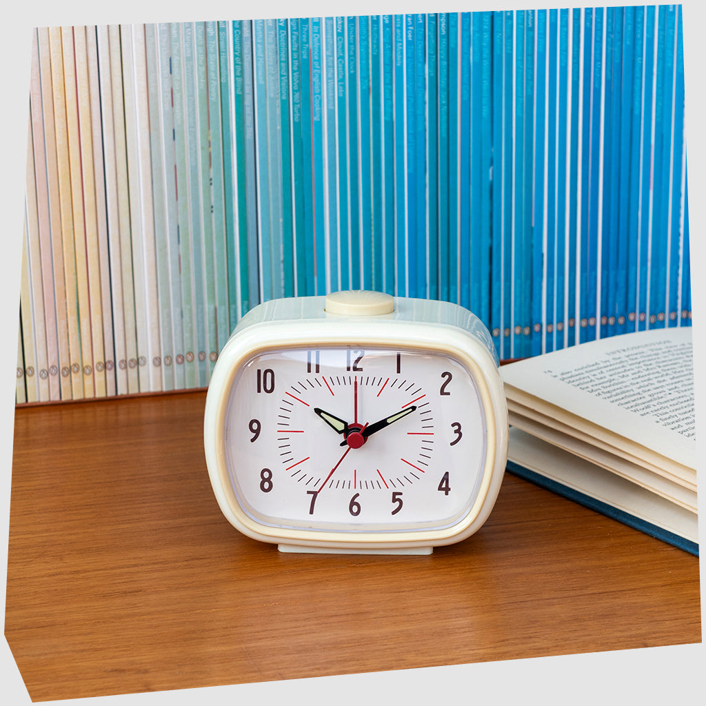 Cream Retro Alarm Clock, by Rex London, with beige numerical dial and casing shown sitting on a bedside table