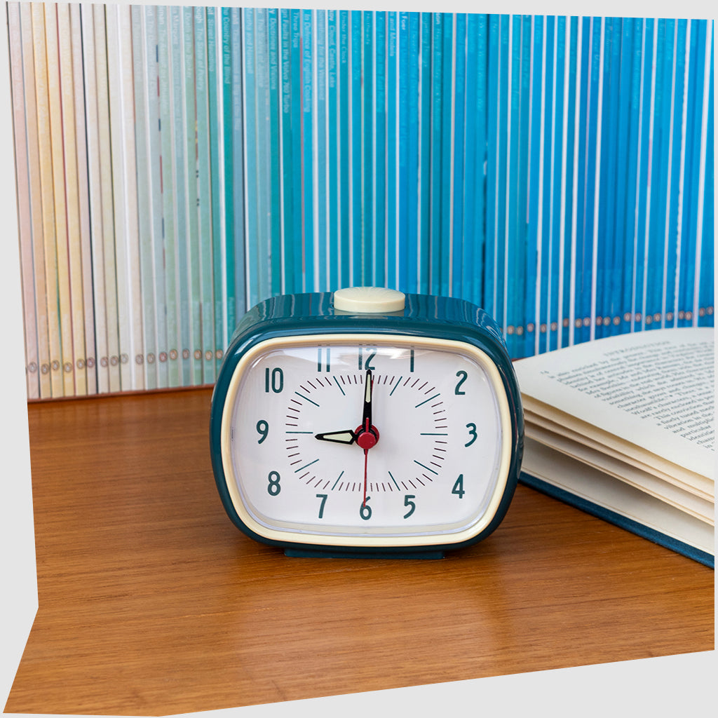 Petrol Blue Retro Alarm Clock, by Rex London, shown on a wooden bedside table