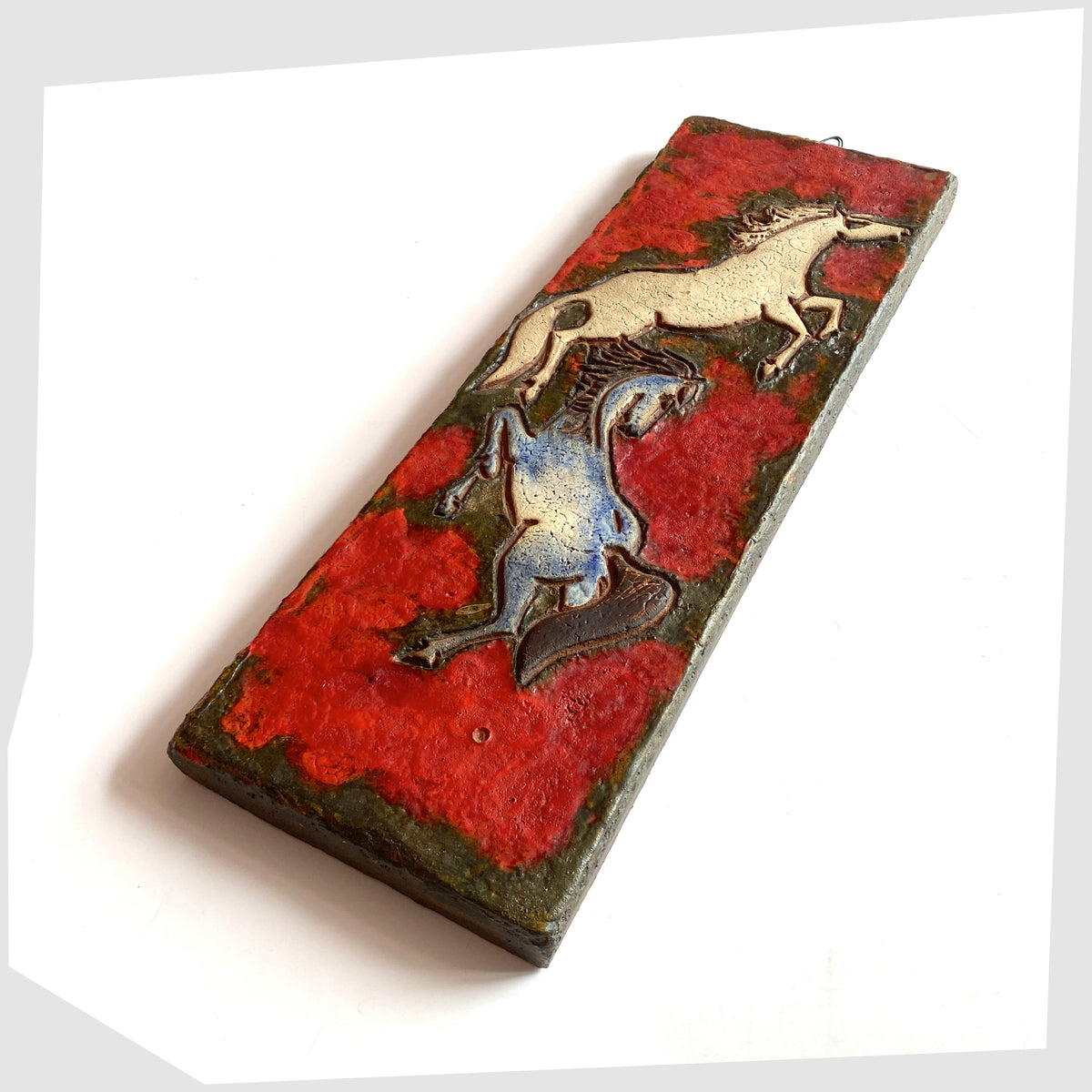 1962 Ruscha Keramik Wall Plaque, designed by Adele Bolz, featuring a pair of horses on a red fat lava glaze, shown on a white background