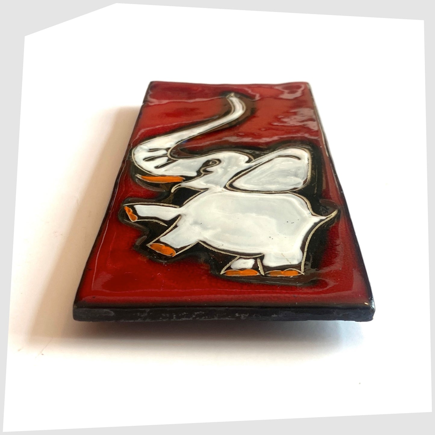 Side profile of the San Marino Pottery Wall Plaque featuring a white elephant with pops of orange on a vivid red glaze, shown on a white background