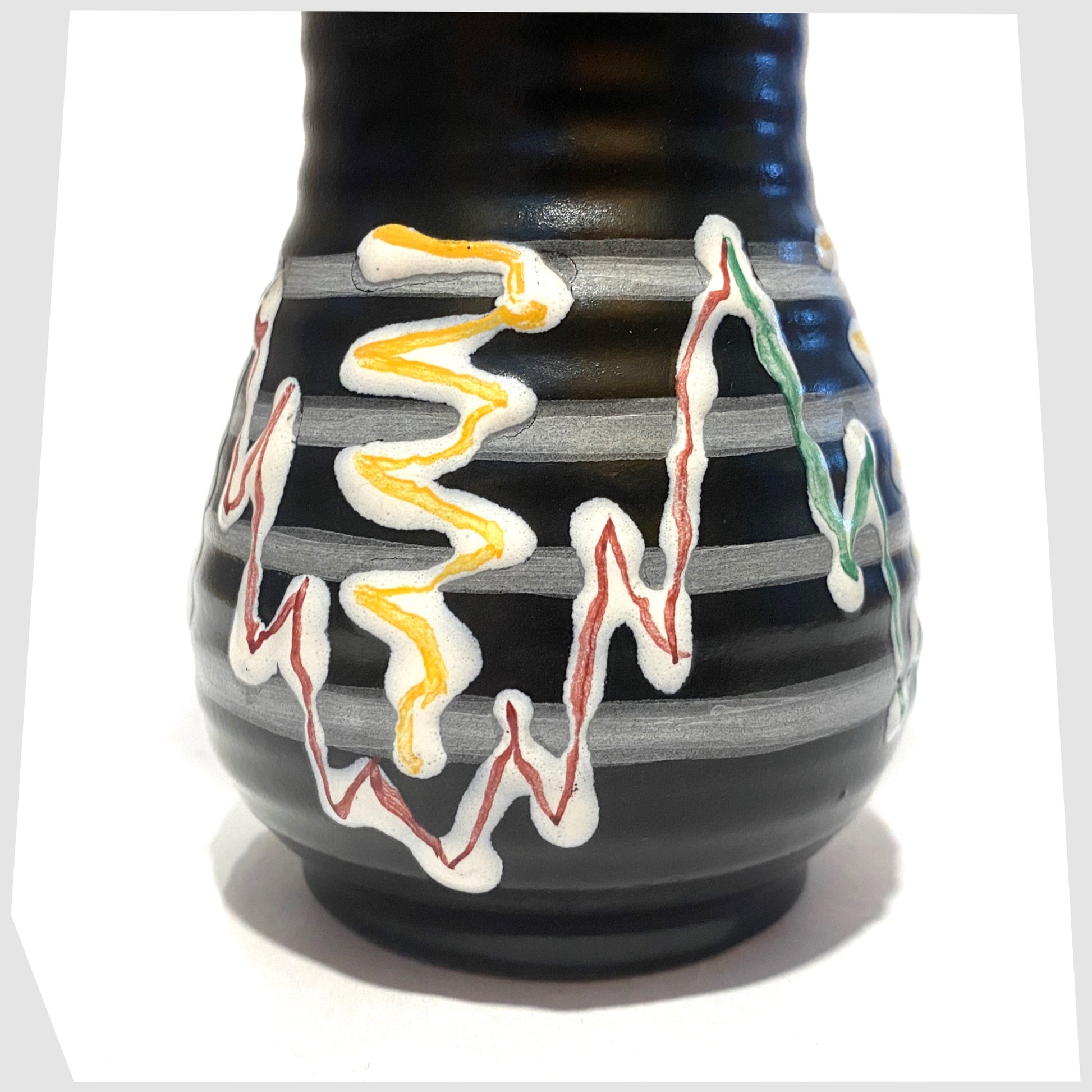 Close up of the black West German Pottery Vase with artistic lines of yellow, green and red glaze, shown on a white background